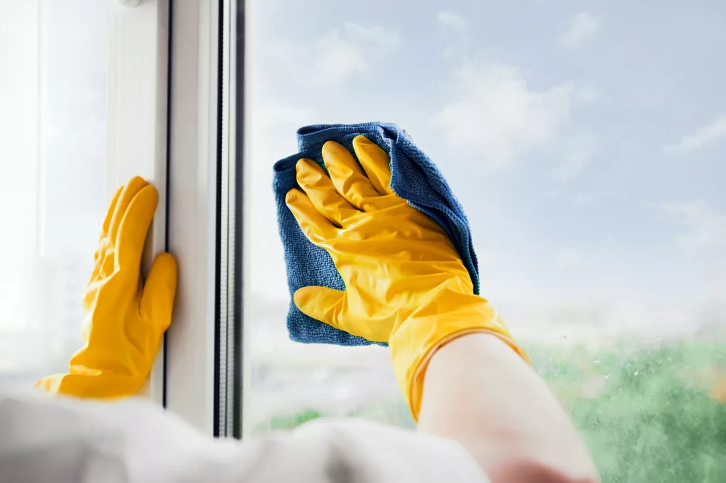 A-Diana cleaning & detail llc offers services of Residential Cleaning, Deep Cleaning, Move Out In Cleaning, Airbnb Cleaning, Construction Cleaning, Office Cleaning, Floor Cleaning, Spring Clean Up, Leaf Removal, Weed Control in Johns creek, Atlanta, Alpharetta, Dunwoody, Conyers, Stone Mountain - Residential Cleaning Man in yellow rubber gloves cleaning window glass with cleaner spray detergent and squeegee